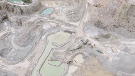 orbital drone shot capturing the earth-moving team working at the bottom of an aggregate quarry with machinery and activity