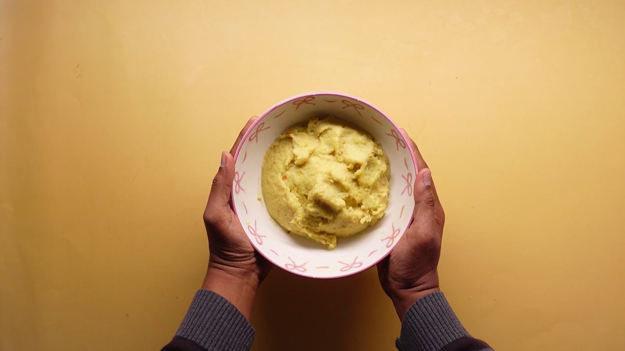 Person Holding Bowl of Mashed Potatoes on Yellow Background