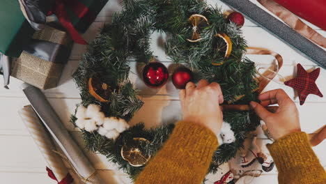 top-view-of-female-hands-holding-Christmas-wreath-with-fir-branches-and-decorative-berries,-with-word-Xmas-on-wooden-tabletop