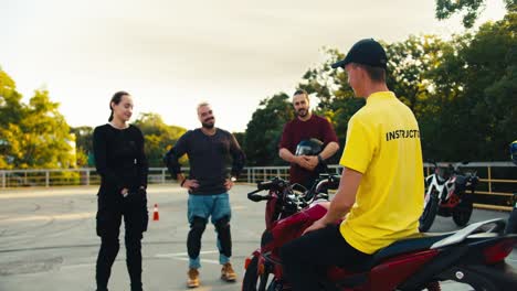 3 estudiantes en la escuela interactúan con un conductor de motocicleta profesional. instructor de conducción en una camiseta amarilla se comunica con los estudiantes