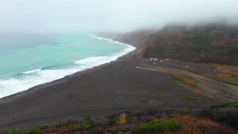 waves black sand 4wd tents rugged coastline usal beach campground lost coast trail california aerial drone fog mist rain cloudy morning pacific ocean pnw nor cali mountainside forward pan up motion