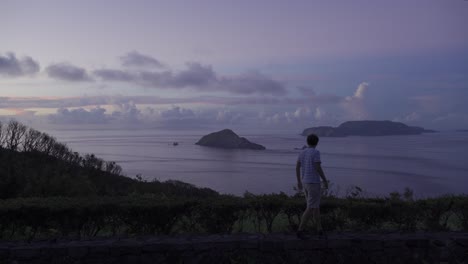 beautiful vista out towards open ocean and silhouetted islands at sunrise with male walking through frame