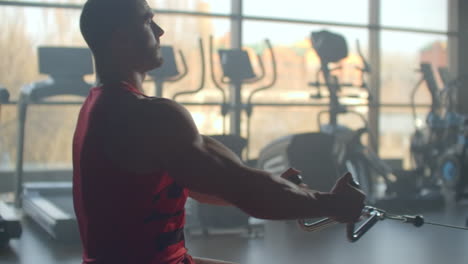 young man doing workouts on a back with power exercise machine in a gym club. at athletic man doing workouts on a back with power exercise machine in a gym on the background of large windows.