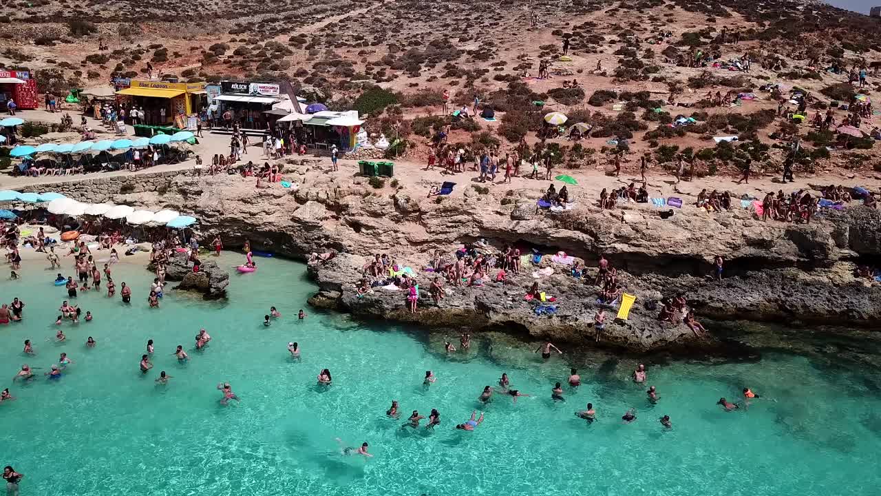 Drone shot of the blue lagoon on Comino Island. Crowded tourist destination, tourists swimming in crystal clear, turquoise water in the high season.