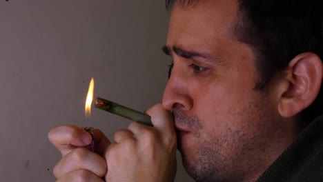 a young man smoking cannabis in a thin pipe. the man lights the tip of the pipe with a lighter, puffs and inhales the marijuana smoke. then blows out cloud of smoke.