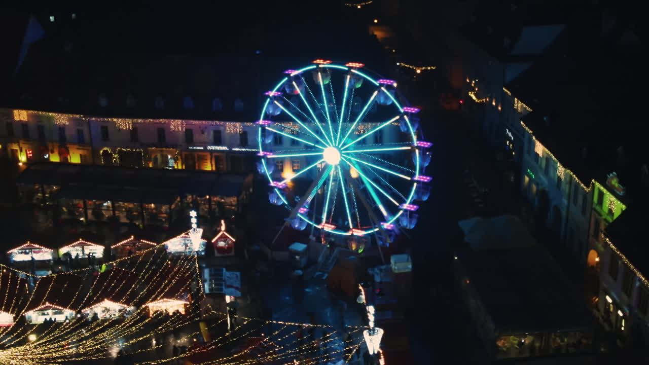Aerial drone view of The Big Square in Sibiu at night, Romania. Old city centre decorated for Christmas. Ferris wheel, old traditional buildings, people