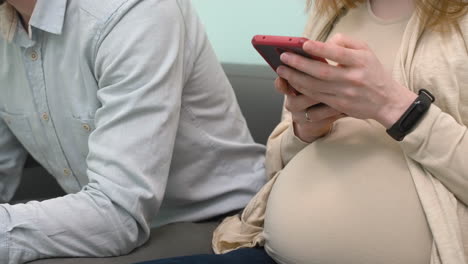 Nahaufnahme-Eines-Schwangeren-Paares,-Das-Im-Wartezimmer-Sitzt-Und-Auf-Dem-Handy-SMS-Schreibt