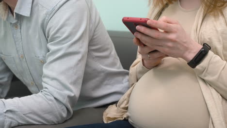 close up of pregnant couple sitting in waiting room and texting on mobile phone