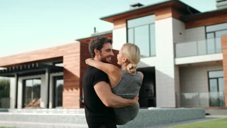 Young-man-holding-woman-near-luxury-house.-Rich-family-hugging-near-new-villa.