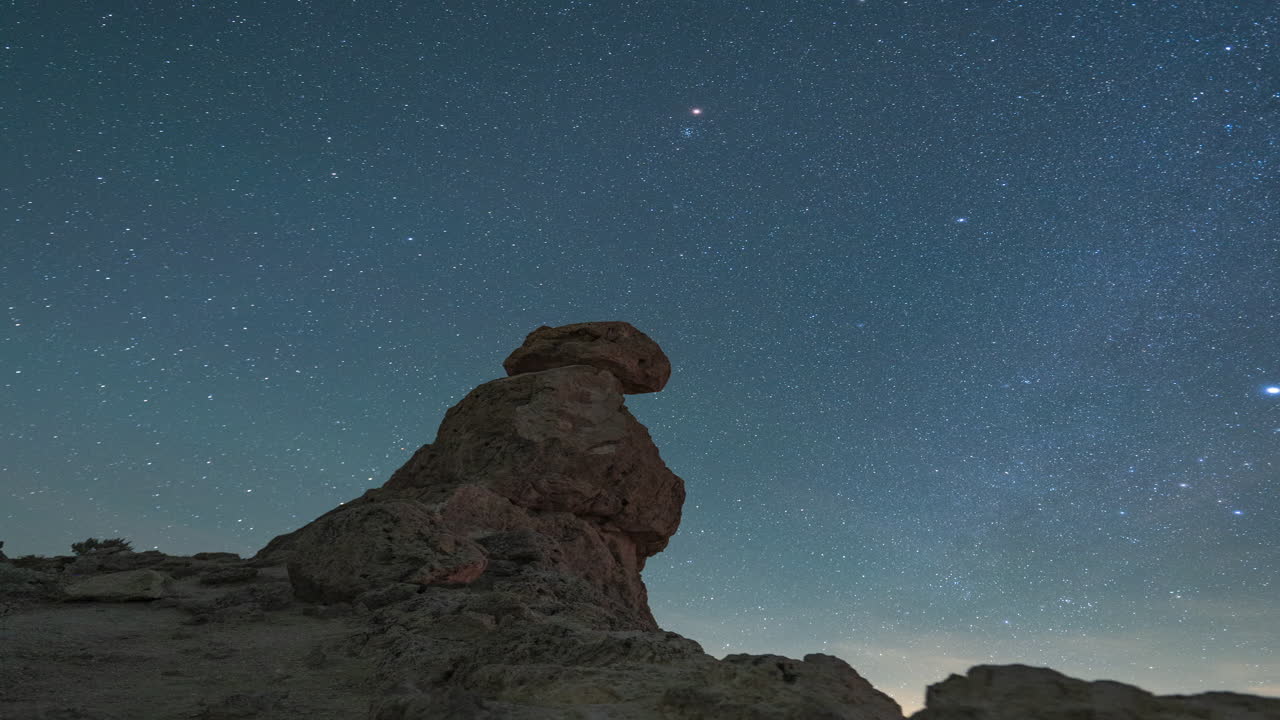 A panning right night timelapse of the starry sky across a rocky desert pinnacle foreground
