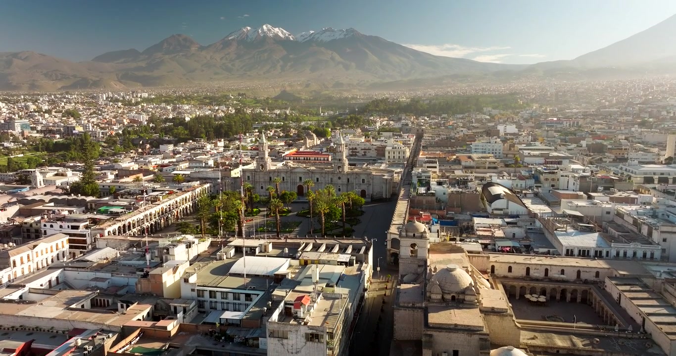 Toma de dron con inclinación ascendente revela la majestuosa Basílica Catedral de Arequipa en Perú. Este icónico monumento de piedra blanca se alza en el centro histórico de la ciudad bajo un cielo soleado, brillante y brumoso.