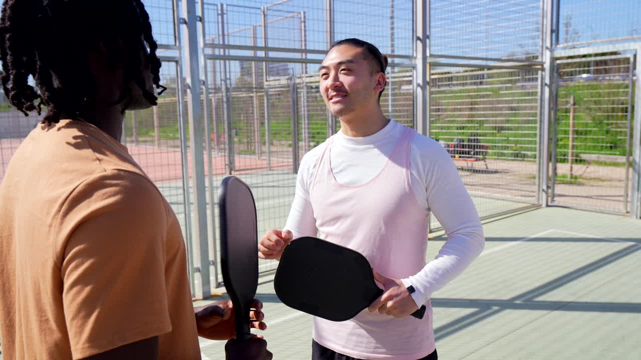 Due uomini di diverse etnie che parlano e si danno il cinque su un campo da pickleball
