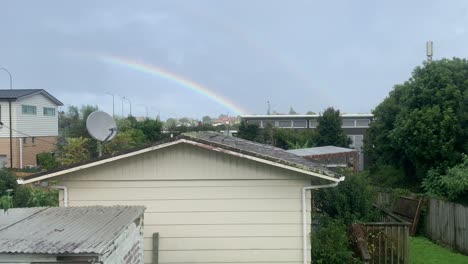 rainbow arch forms in a cloudy sky above houses in auckland new zealand