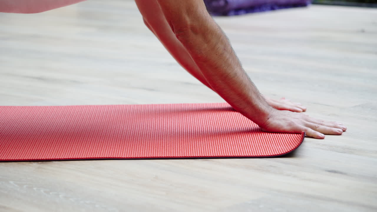 Nærbilde av hender som ruller ut en rød yogamatte på tregulv