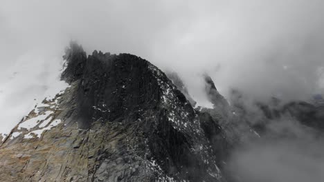 aerial view entering the fog with a rocky and sharp ridge in the andes on a cloudy day