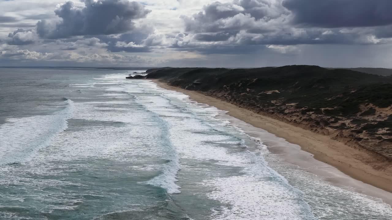 Drone camera glides above Portsea shoreline, capturing dramatic waves, rugged coast, and moody skies