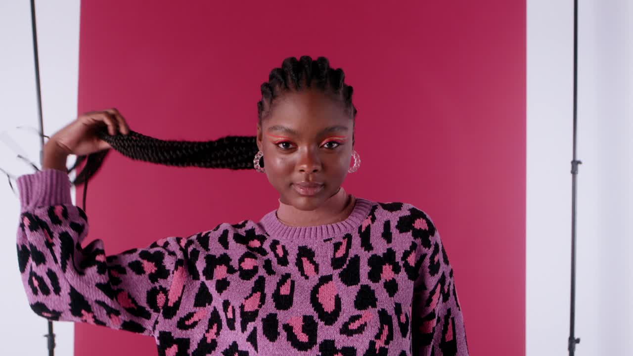 Black woman poses looking at the camera, smiling as she holds her beautiful tied-back black hair and moves her arms gracefully