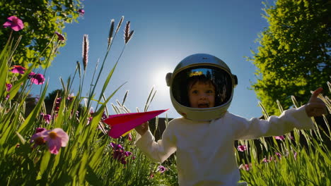 a child in an astronaut helmet plays with a paper airplane and a sparkling toy rocket in a sunny garden