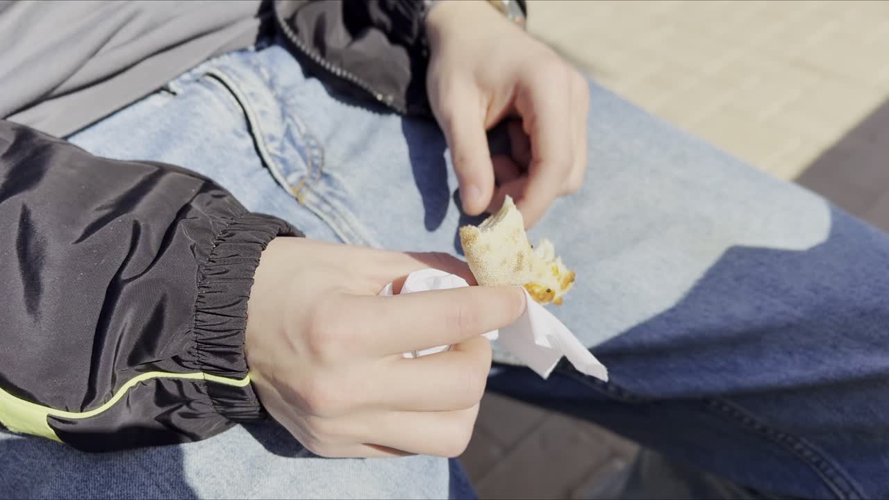 Primo piano di una persona con giacca e jeans neri che si gusta un pezzo di pane pita fresco seduta all'aperto. Uno scatto spontaneo che cattura una rapida pausa snack alla luce naturale del sole.