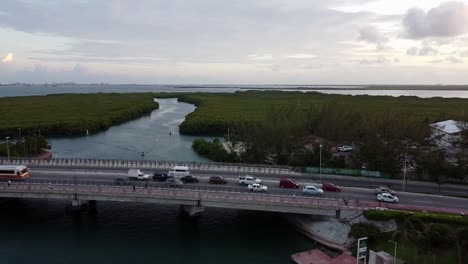 zoom out of a bridge above of underpass lagoon while car driving at sunset time