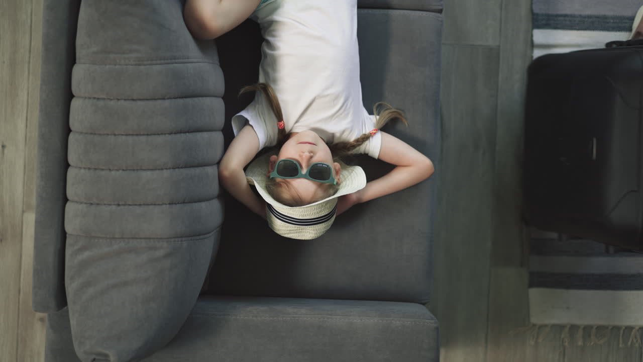 la mano de la madre tomando la maleta mientras la niña descansa en el sofá