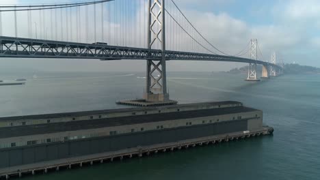 Toma-Aérea-De-Vehículos-Moviéndose-En-El-Puente-De-La-Bahía-De-San-Francisco–oakland-Con-La-Ciudad-Al-Fondo