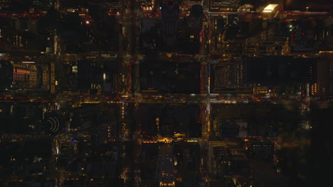 Aerial-birds-eye-overhead-top-down-static-shot-of-night-downtown.-Traffic-in-illuminated-streets-between-blocks-of-buildings.-Manhattan,-New-York-City,-USA