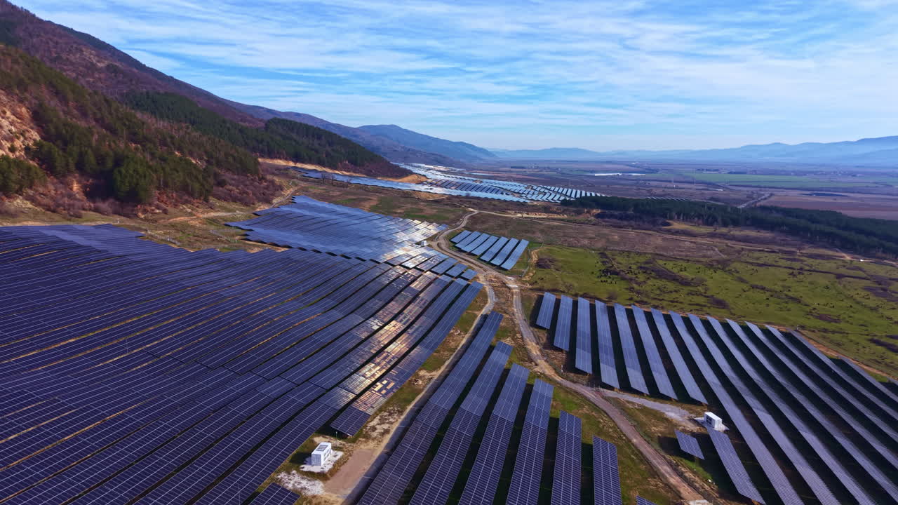 Solpaneler dækker et stort område i en dal på en solrig dag, der viser brug af vedvarende energi nær bjerge