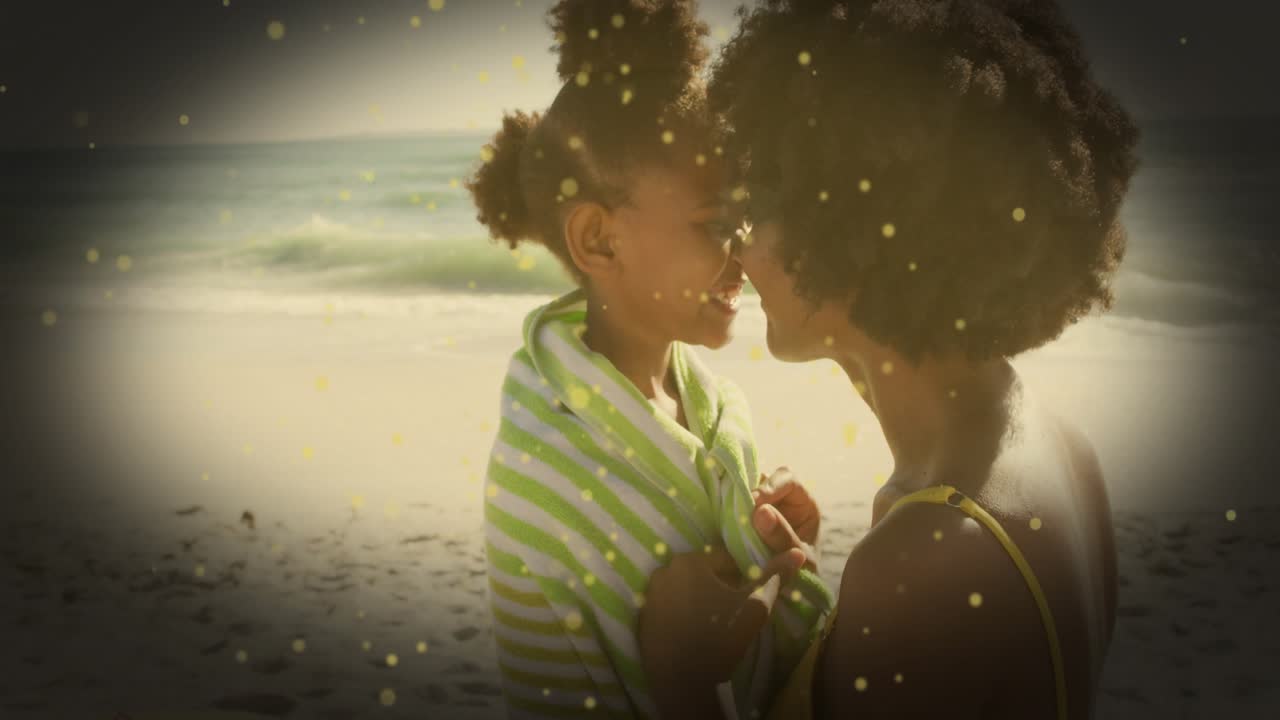 Mom wrapping towel around daughter on beach after swim soothing gold sparks around them for family
