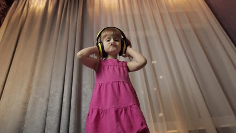 Little-child-girl-in-wireless-headphones-enjoying-listen-music.-Dancing-at-home