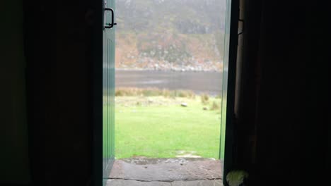 a man with dreadlocks and wearing hiking gear is sitting on a step in a narrow doorway of a bothy in the highlands of scotland before standing up and walking into a dark room