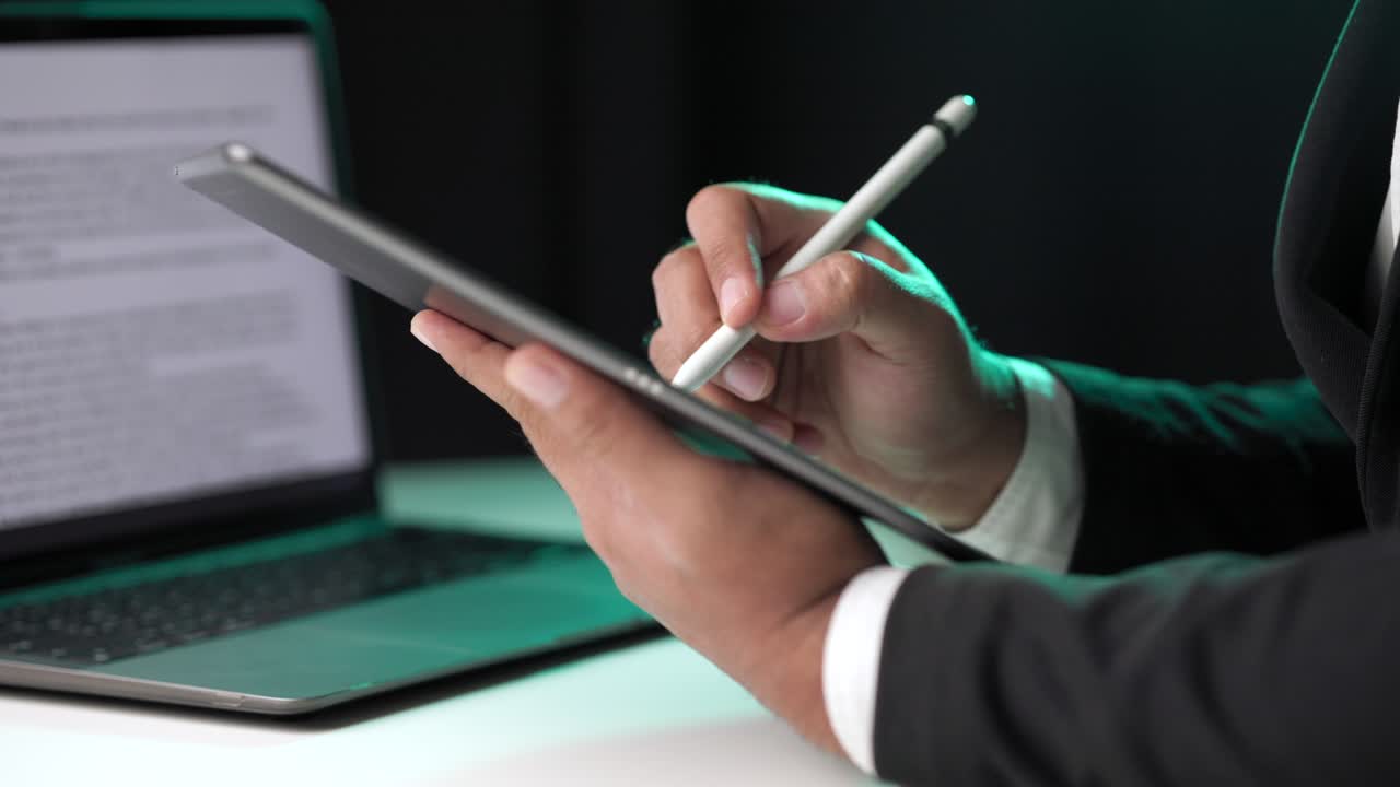 Electronic signature with green light. Businessman signing a business contract with stylus pen on tablet at night. Man signing contract on tablet at office. Business and technology concept.