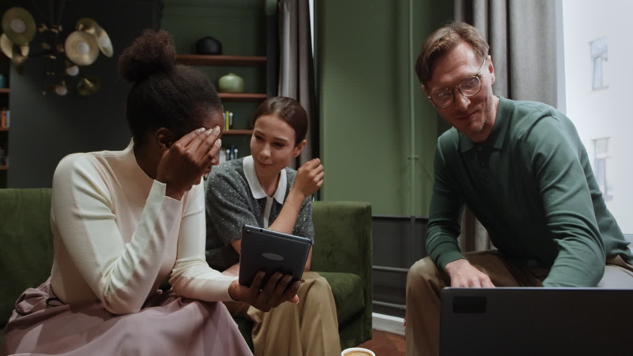 Three diverse colleagues collaborating with digital devices in an office lounge