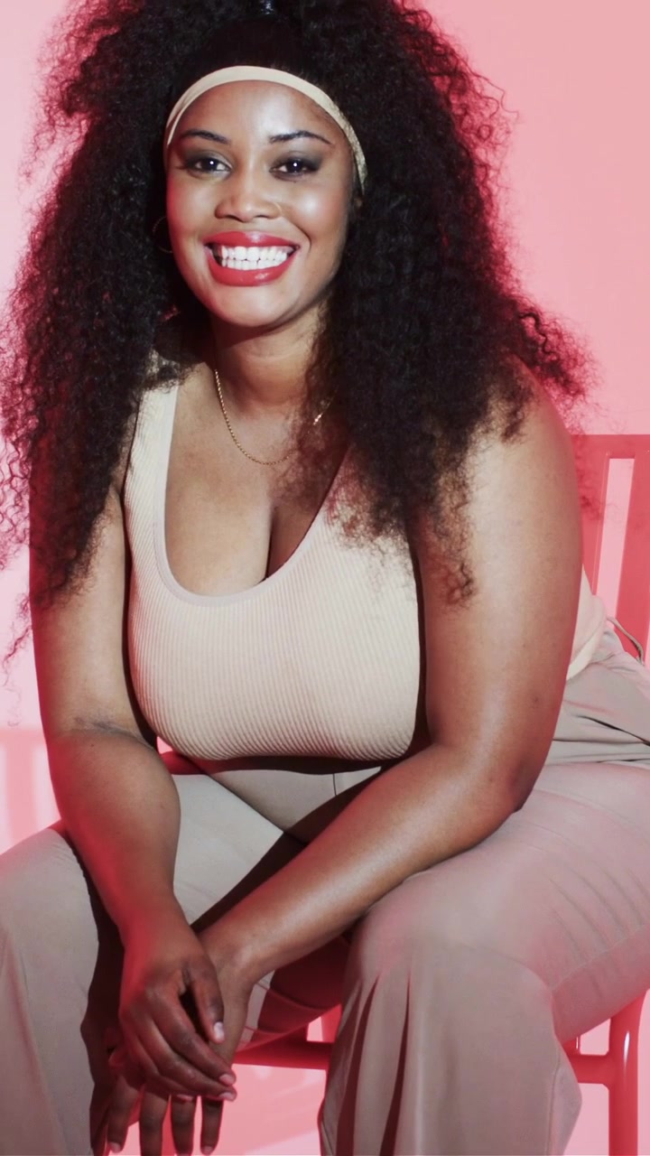 Vertical video: Posing on camera woman wearing beige top lifting chin then smiling on pink backdrop