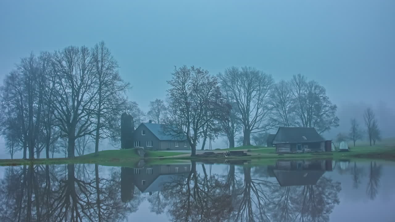 코티지 하우스와 헛간이 있는 호수 위의 안개 낀 공기의 시간 경과