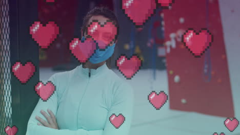 iconos de corazón rosado flotando contra contra retrato de mujer en forma caucásica usando una máscara en el gimnasio
