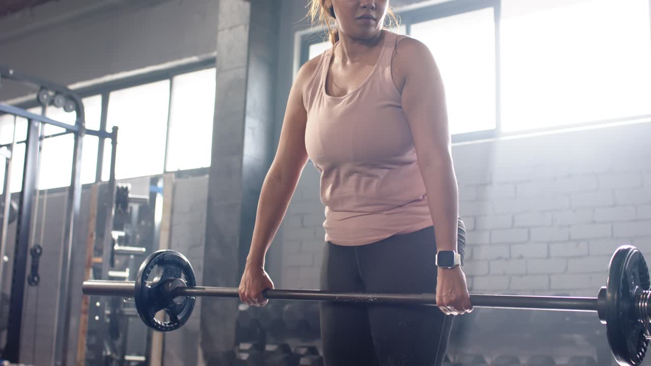 Donna che entra in palestra, solleva pesi e afferra il bilanciere con i dischi, impegnando il core per lo stacco da terra