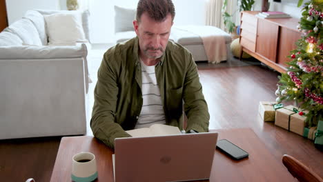 man working on laptop at home near christmas tree, deep in thought