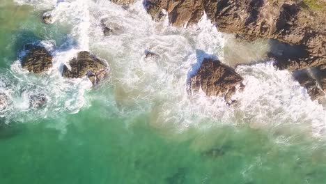 aerial top-down shot of waves crashing against rocky shore in byron bay, showcasing the natural power of the ocean