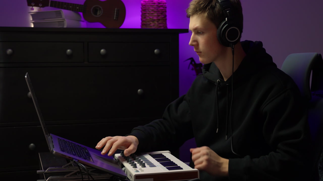 A DJ sampling on his MIDI keyboard then syncs it on the laptop in a home studio, closeup