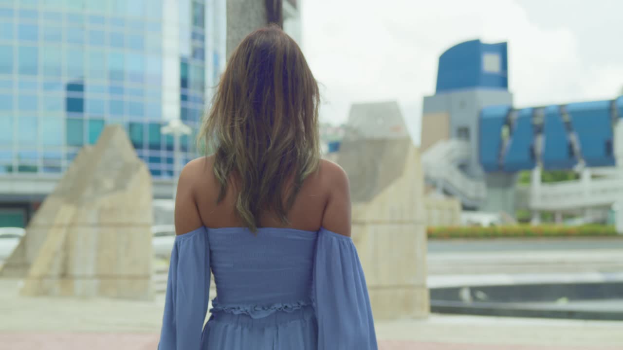 도시에서 파란 드레스를 입고 야자수에 기대기 전에 도시를 걷는 여자