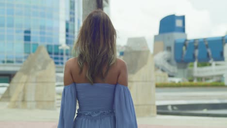 a woman walking in the city before leaning on a palm tree while wearing a blue dress in the city