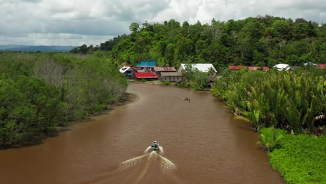 aerial flight tracking moving boat in murky village river in indonesia