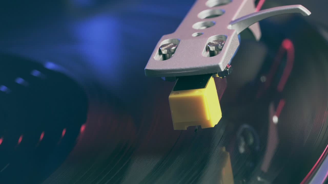 빨간색과 파란색의 불빛을 배경으로 한 비닐 회전판의 클로즈업. 회전하는 검은 비닐 레코드 플레이어의 조각.