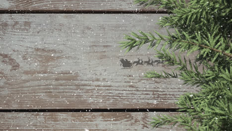 tree branches and santa claus in sleigh being pulled by reindeers against wooden plank