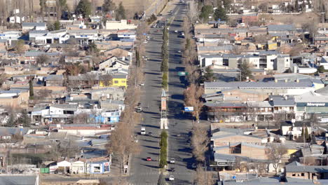 drone establishing shot of avenida san martín, the main avenue in malargüe, province of mendoza, argentina, with bare winter trees, urban buildings and light traffic