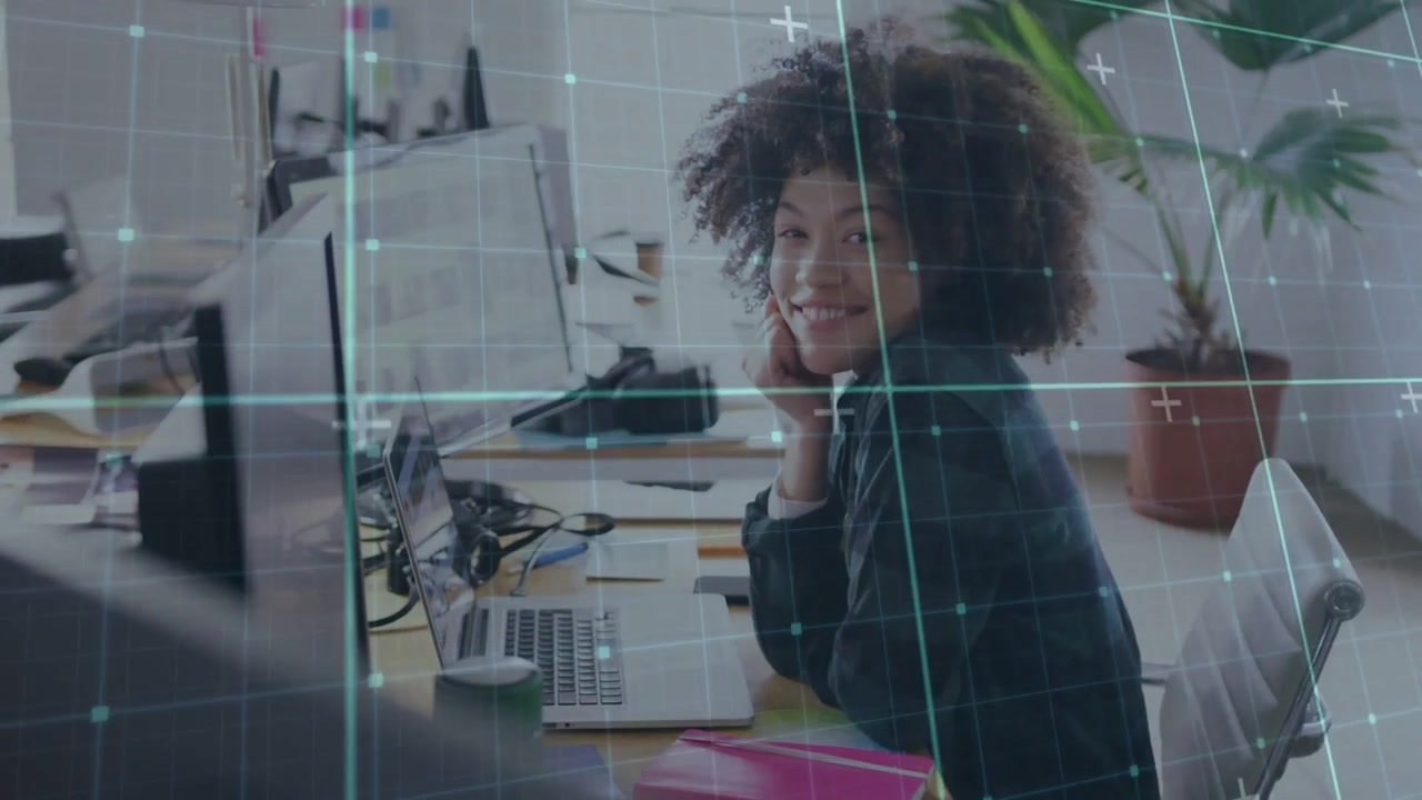Woman typing in business office, pausing then turning and engaging camera as grid overlaying laptop