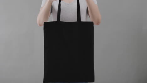 mujer caucásica con camiseta blanca sosteniendo una bolsa negra sobre un fondo gris, espacio de copia, cámara lenta