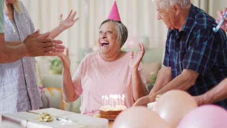 happy senior biracial woman having birthday party and cake with diverse senior friends, slow motion