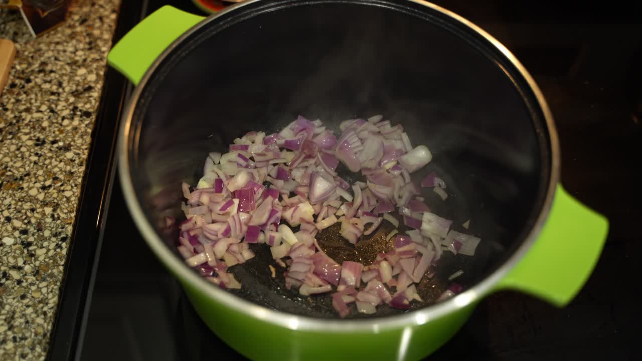 Chopped onions cooking in a metal pot on the stove in closeup with steam coming from pot